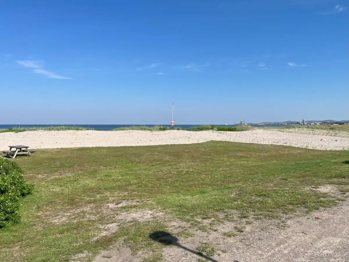 Gräsyta och sandstrand vid campingen med havet bakom